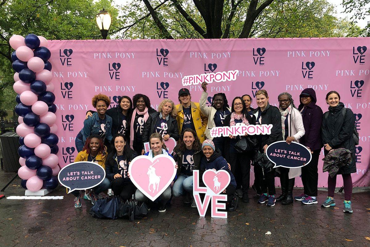 Personas reunidas frente a un gran cartel rosado que dice Pink Pony Walk 2019