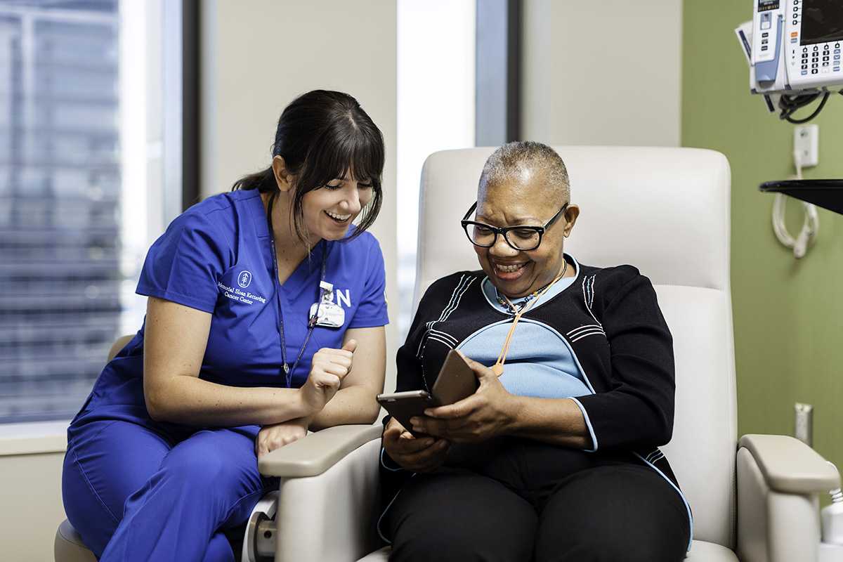 A registered nurse shares a laugh in an exam room with a patient as they both look at a cell phone screen. 