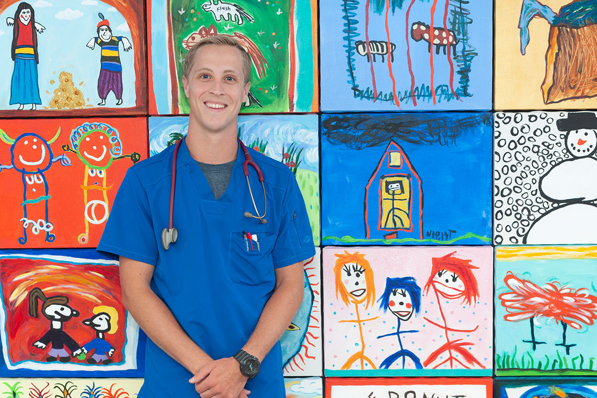 Kurt MacDonald standing in front of a wall with drawings done by children