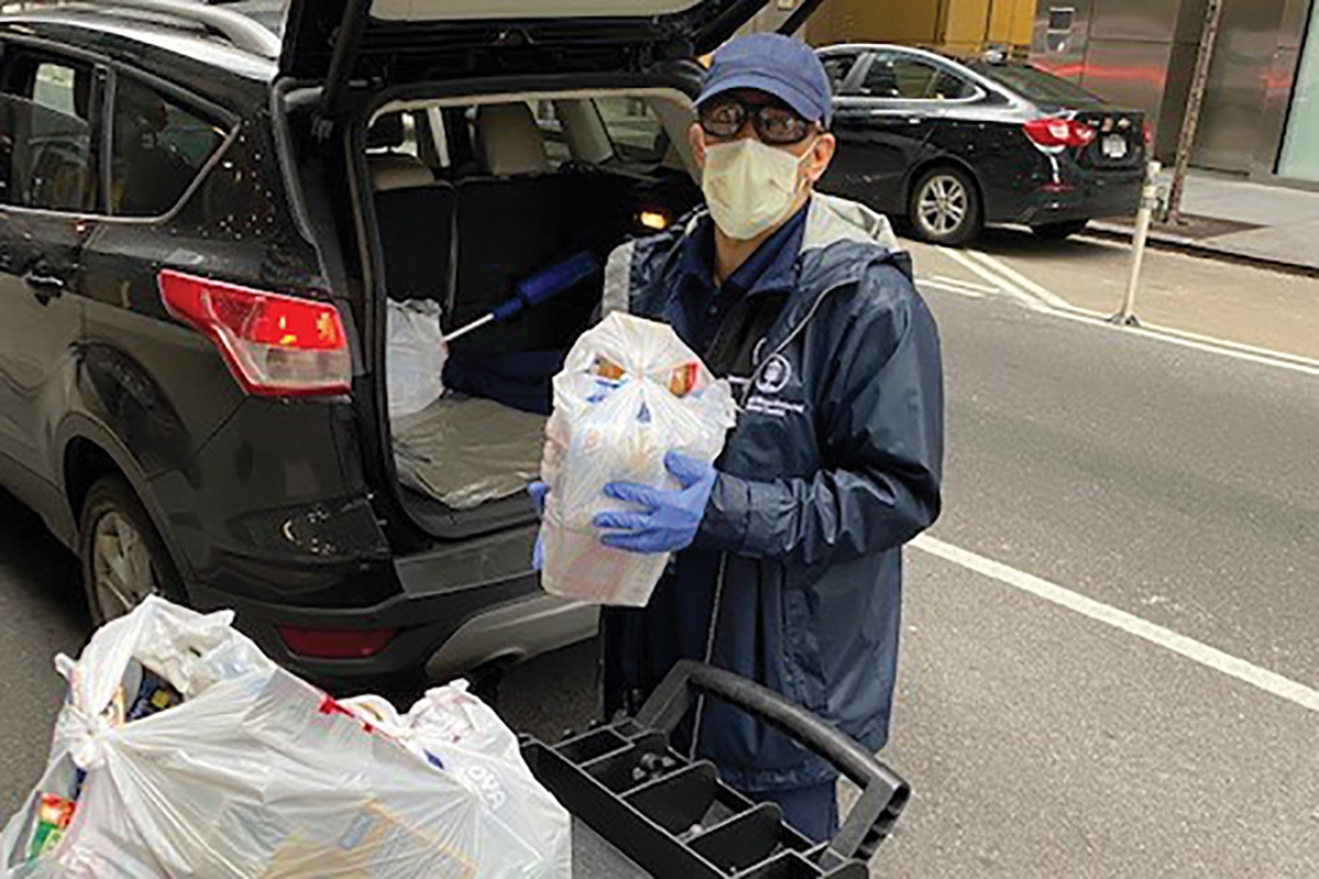 Man wearing a mask and holding a bag of groceries outside by a car
