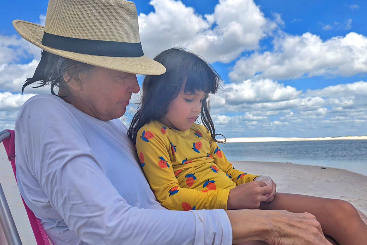 Older woman on beach with girl in her lap.