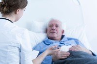 Old man lying in hospital bed being spoken to by nurse