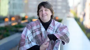 Person smiling on an outdoor terrace while wearing a pink plaid shawl.