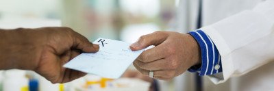 Patient hand giving prescription slip to pharmacist’s hand.