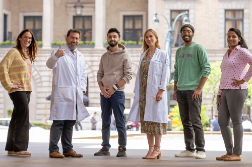 Four people who were successfully treated for rectal cancer in a clinical trial at Memorial Sloan Kettering are seen posing outdoors with the trial’s two principal investigators. 