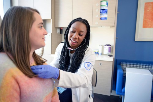 Dr. Alexis Chidi examining thoracic patient with stethoscope. 